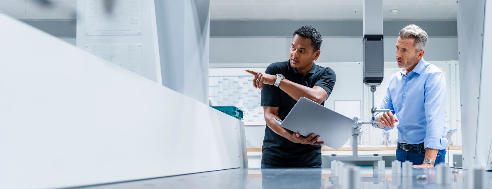 Engineer with laptop pointing by businessman at factory